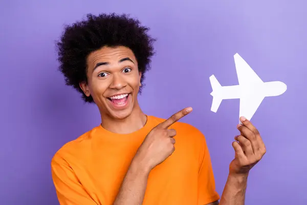 Photo of crazy funky young tourist guy directing forefinger demonstrate boeing airplane paper model isolated on purple color background.