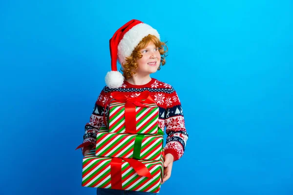 甜美梦幻般的小男孩头戴装饰毛衣圣诞礼帽 手里拿着礼物 看起来空荡荡的 孤零零的蓝色背景 — 图库照片