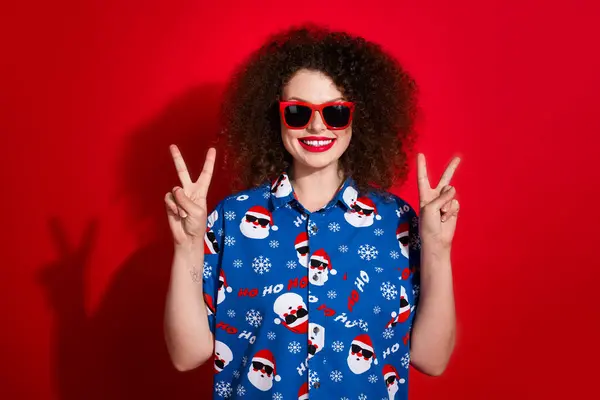 迷人的年轻女子的照片肖像 她的双拇指向上竖起 穿着时髦的蓝色圣诞印花衣服 与红色背景隔离 — 图库照片
