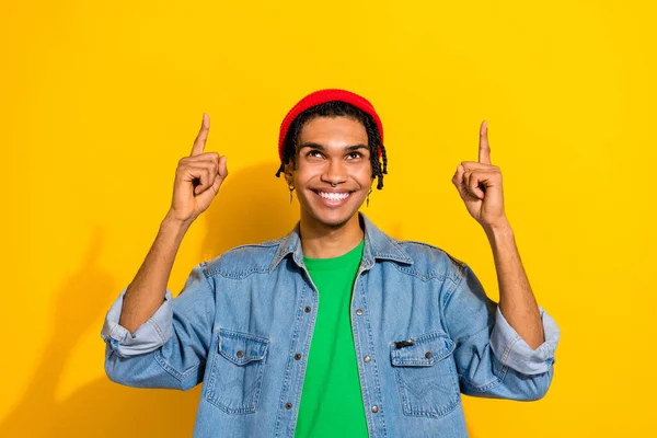 Photo of funky nice guy man wear stylish denim clothes piercing earrings two arms direct empty space isolated on yellow color background.