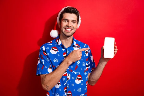 鮮やかな赤色の背景で隔離されたスマートフォンタッチスクリーンで監督サンタハットブルーシャツを着た陽気な人の肖像 — ストック写真