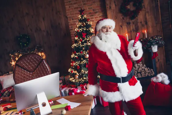照片上喜庆积极的圣诞老人穿着红色服装在室内迎接苹果Iphone三重唱设备北极星回家 — 图库照片