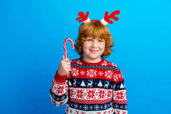照片中狡猾有趣的小男孩穿着华丽的装饰毛衣角享受着圣诞糖果手杖蓝色的背景 — 图库照片
