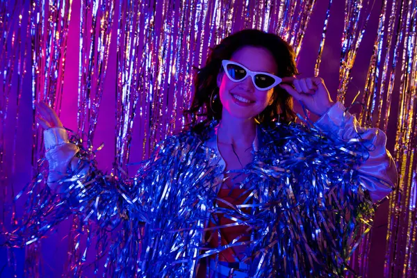 兴奋而时髦的女士穿着金银花夹克深色眼镜 有着迪斯科式有趣的孤立霓虹灯紫色背景的照片 — 图库照片