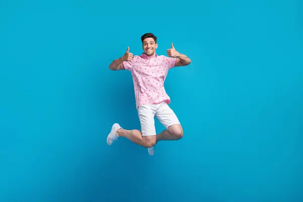 Full length photo of excited sporty person jumping hands fingers demonstrate thumb up isolated on blue color background.