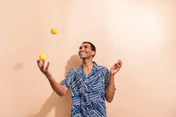面白い陽気な男の写真 プリントシャツを着て笑顔のジャグリングレモン隔離ベージュ色の背景 — ストック写真