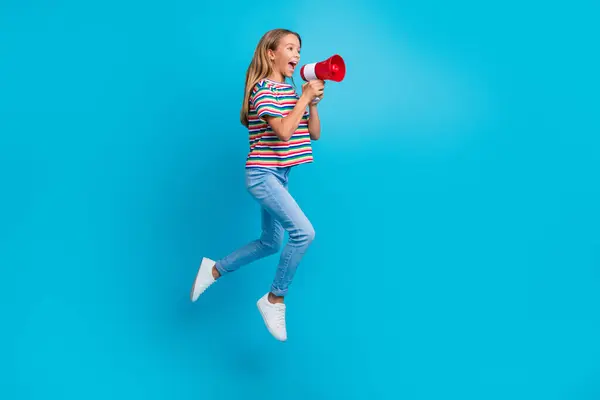Full length photo of active schoolgirl dressed striped t-shirt jumping announcing sale in empty space isolated on blue color background.