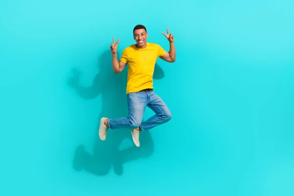 興奮するファンキーな男のフル長さの写真 黄色のTシャツのジャンプ高く2つのVシグナル隔離されたターコイズ色の背景を示す — ストック写真