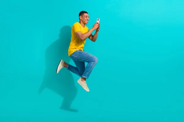 興奮したハンサムな男のジャンプの完全な長さのプロフィールの肖像画はターコイズ色の背景で隔離されたスマートな電話の空のスペースを使用します — ストック写真