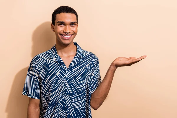Photo of cheerful positive guy dressed print shirt showing arm empty space isolated beige color background.