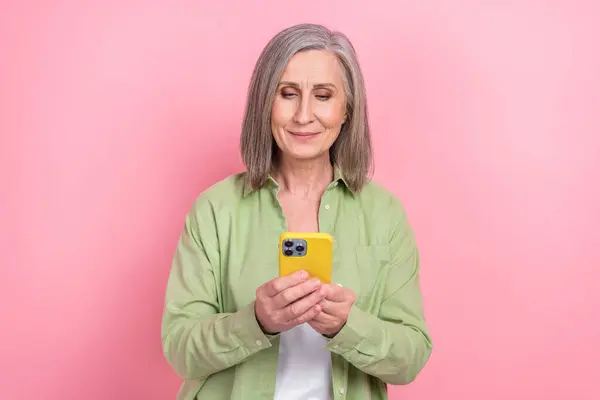 退休女性博客的照片 穿着卡其布衬衫 手持智能手机学习新设备指令 与粉色背景隔离 — 图库照片