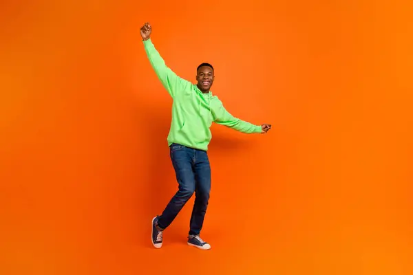 Full body photo of carefree good mood guy dressed green hoodie denim pants raising hands up win bet isolated on vivid orange background.