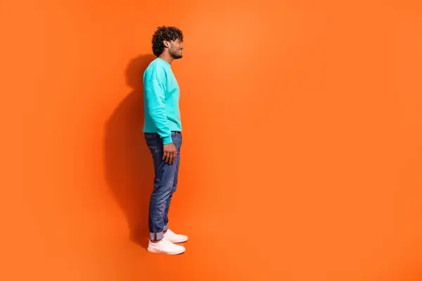 Full length side profile shot of arabian guy wearing casual outfit looking interested brands outlet isolated on orange color background.