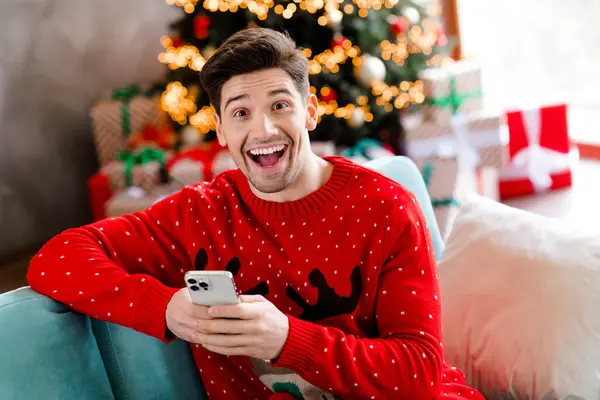 ハンサムな驚いた人の写真 開いた口ソファー スマートフォンチャット クリスマスタイム魔法屋内 — ストック写真