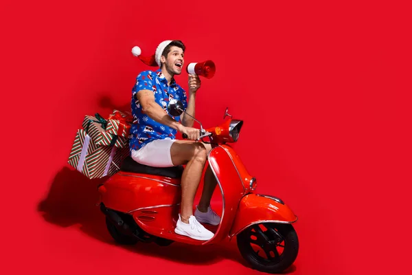ファンキーな若い男性ドライブのフルサイズの写真 モペットメガフォンドレスサンタクロースプリントXマス服 赤い色の背景で隔離 — ストック写真