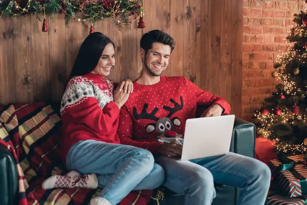 Photo of positive two people friends browsing laptop to click website page order gifts sitting divan waiting santa claus delivery indoors.