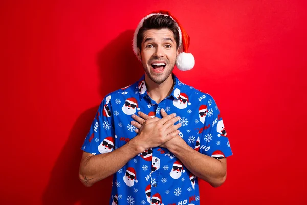 エクスタシーな男の写真は 鮮やかな赤い色の背景で隔離された見ている胸に腕を保持するクリスマスの帽子のプリントシャツを着用します — ストック写真