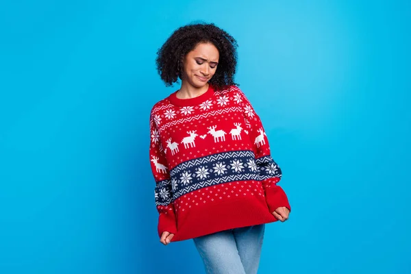 Photo of young girl grimace and showing her oversize ugly sweater which she wearing every christmas isolated on blue color background.