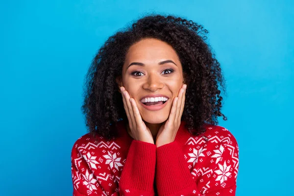 Portrait of excited girl dressed ugly red print pullover arms cheeks smiling shocked see santa claus isolated on blue color background.