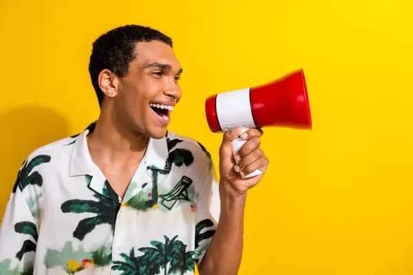 Photo of eccentric man with piercing dressed palm print shirt scream in loudspeaker at empty space isolated on yellow color background.