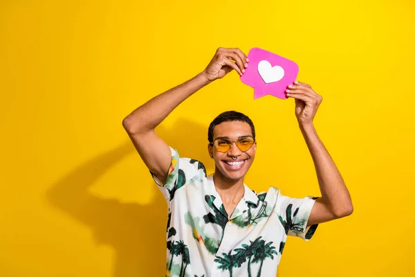 Photo of cheerful cool guy dressed stylish clothes arms above head showing pink paper card isolated on vivid yellow color background.