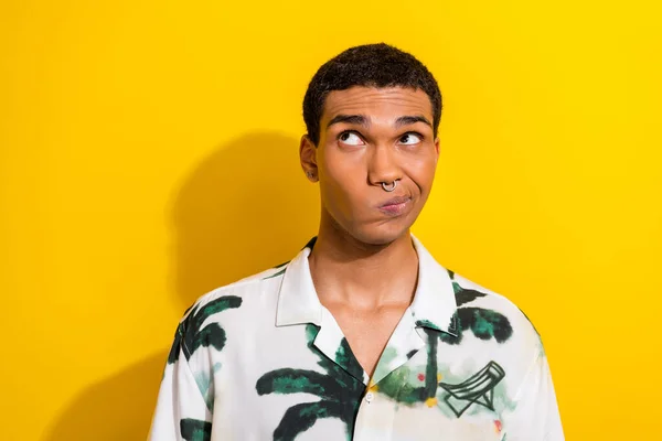 Photo of funky minded man with nose piercing dressed palm print shirt thoughtfully look empty space isolated on yellow color background.