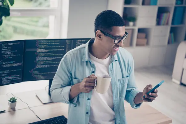 照片中的年轻人成功程序员它的专家浏览智能手机喝早上卡布奇诺咖啡在办公室桌面上的工作空间 — 图库照片