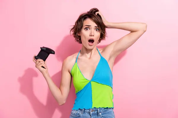 Photo of young model girl wear stylish green tank top touch head player video games using joystick loose isolated on pink color background.