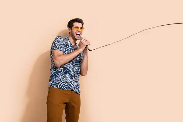 Photo of cheerful crazy guy dj music lover dressed trendy clothes singing hit looking empty space isolated on beige color background.
