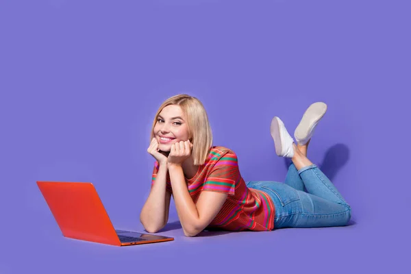 Full body photo of student girl choosing movie for halloween night party entertainment on laptop isolated over purple color background.