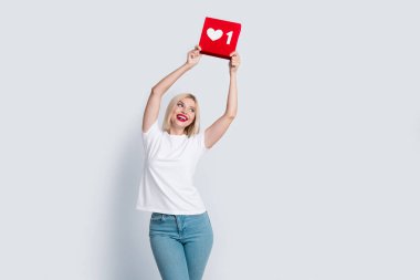 Portrait of good mood girl with blond hairdo wear t-shirt look at social media like in hands over head isolated on gray color background. clipart