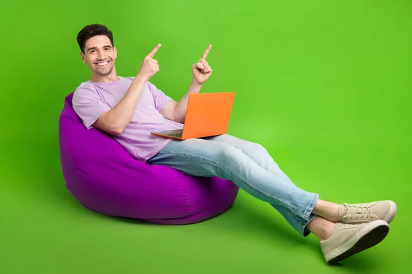 Full length photo of successful man dressed stylish clothes sitting soft chair presenting empty space isolated on green color background.