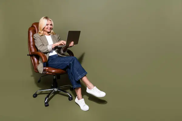 全长照片 金发碧眼的女性电子邮件营销专家坐在椅子上 在卡其色背景下使用独立的上网本 — 图库照片