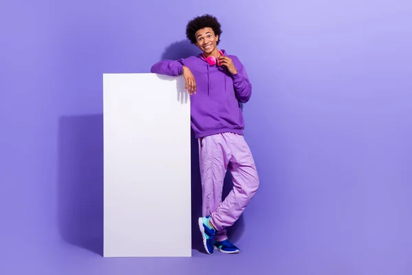 stock image Full length photo of positive guy dressed pullover lean on smartphone screeen touching headphones isolated on violet color background.