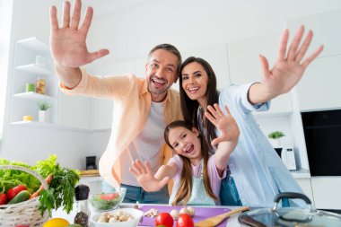Photo of funky sweet married couple small daughter waving palms hi cooking dinner together indoors home kitchen. clipart