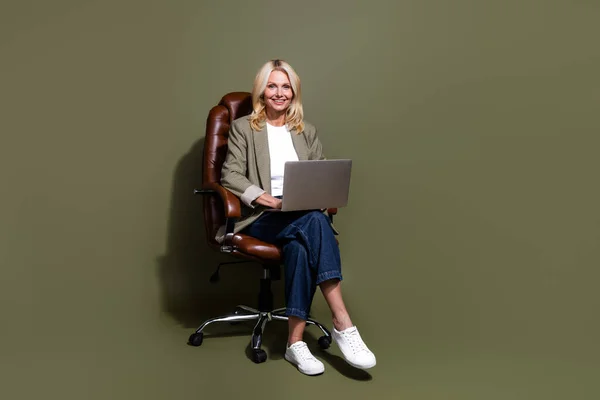 全身上下都是笑容满面的商务女士与电脑老板坐在扶手椅上 在卡其色背景下举行在线会议 — 图库照片