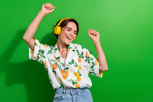 Photo of young girl brown bob hair wearing stylish spring season shirt raised fist up enjoy earphones isolated on green color background.