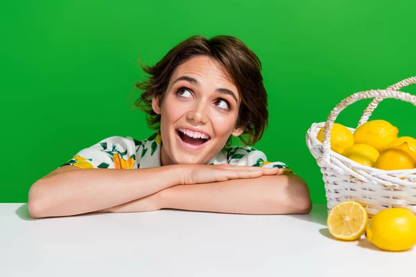 Photo of young lady folded hands on table surprised lady collect fresh lemons looking empty space isolated on green color background.