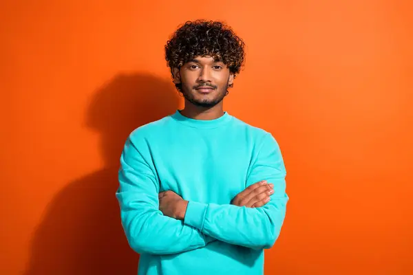 Portrait of young leader guy wearing stylish turquoise sweatshirt folded hands feel self confidence isolated on orange color background.