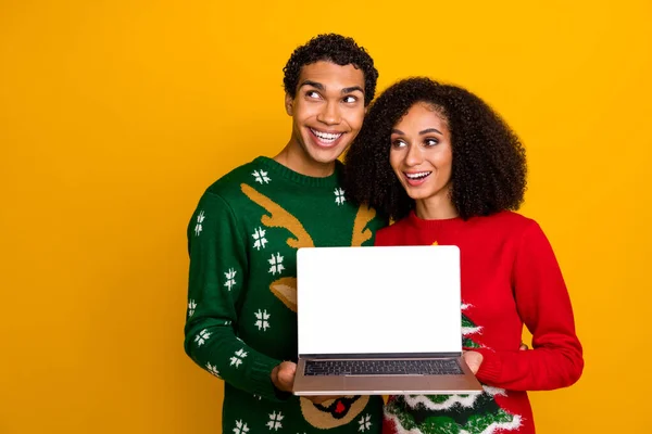 Portrait of two funny people hold show netbook display eshop offer look empty space isolated on yellow color background.