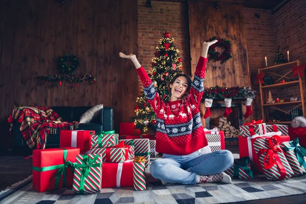 漂亮的年轻女子坐在地板上举起双手精力充沛地穿上红色毛衣圣诞节房间室内设计树装饰在室内 — 图库照片
