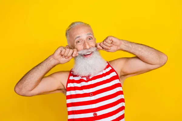 Photo of positive excited elderly guy dressed striped red swimsuit adjusting hands arms mustaches isolated yellow color background.