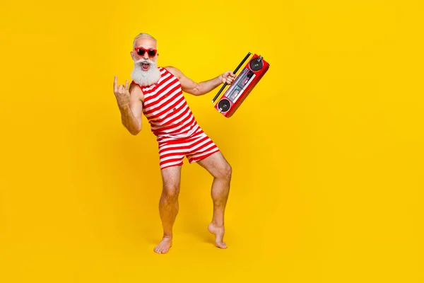 Full length photo of aged man in swimsuit positive singing metal rock roll brutal music holding boombox isolated on yellow color background.