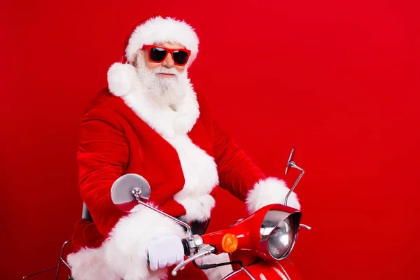 Full size photo of cool positive grandfather wear stylish santa costume glasses travel on red scooter isolated on red color background.