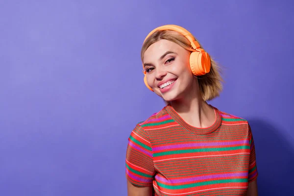 ヴァイオレットカラーの背景に隔離された新しいワイヤレスヘッドフォンに関するストライプTシャツの自慢の美しい少女の写真の肖像画 — ストック写真
