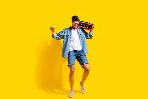 Full body photo of positive man dressed denim shirt shorts in glasses dance with boombox enjoy music isolated on yellow color background.