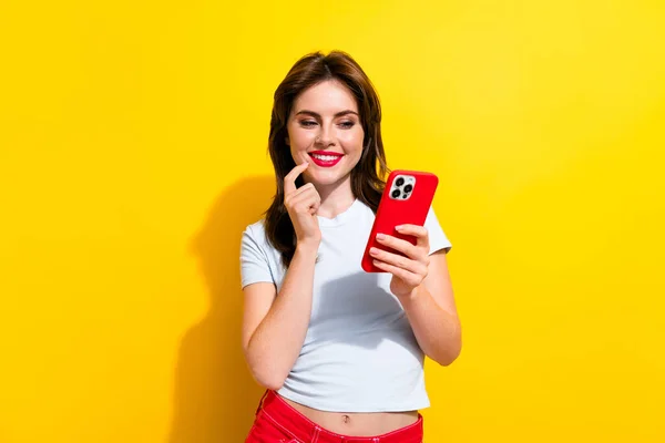 Photo of minded smart cheerful woman dressed white t-shirt look at smartphone read notification isolated on yellow color background.