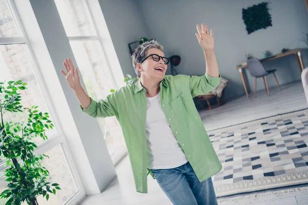 Photo of carefree laughing funky lady mature age raised palms up enjoying weekend atmosphere in living room bought new apartment today.