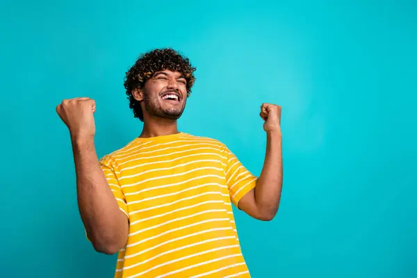 Photo of satisfied delighted man closed eyes raise fists attainment luck empty space isolated on teal color background.
