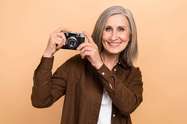 Photo of nice satisfied aged person toothy smile hands hold retro photo camera isolated on beige color background.